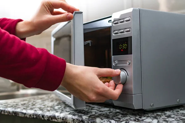 Woman\'s hand closing the door of the microwave oven and sets the time for heating food