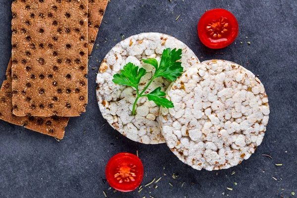 Rye, wheat crisp bread and rice bread, cherry tomatoes and fresh parsley on a dark background. Snack Bread. Top view