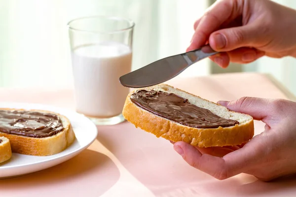 Spread chocolate paste on freshly baked bread. Chocolate sandwiches with nut, sweet paste and a glass of milk for a breakfast.