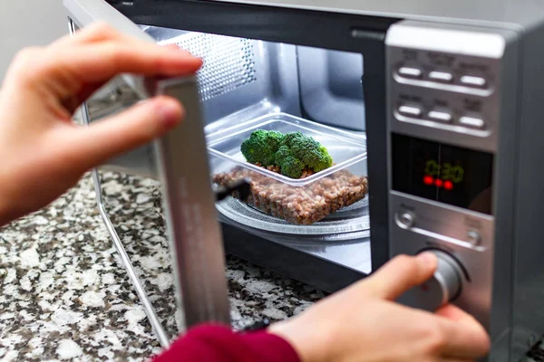 Woman\'s hand closing the door of the microwave oven and sets the time for heating food