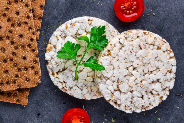 Rye, wheat crisp bread and rice bread, cherry tomatoes and fresh parsley on a dark background. Snack Bread. Top view