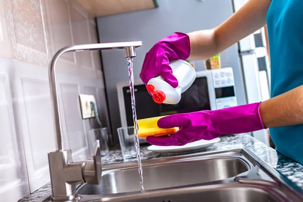Housewife in rubber colored gloves washing dishes with a yellow sponge in the kitchen at home.