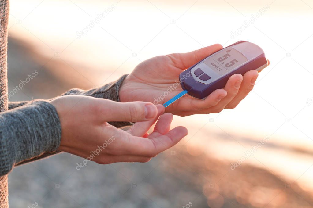 A diabetic is testing blood glucose levels on the beach at sunset. Diabetes lifestyle, diabetic vacation at sea. Diabetes is not a hindrance to rest and an active, healthy lifestyle