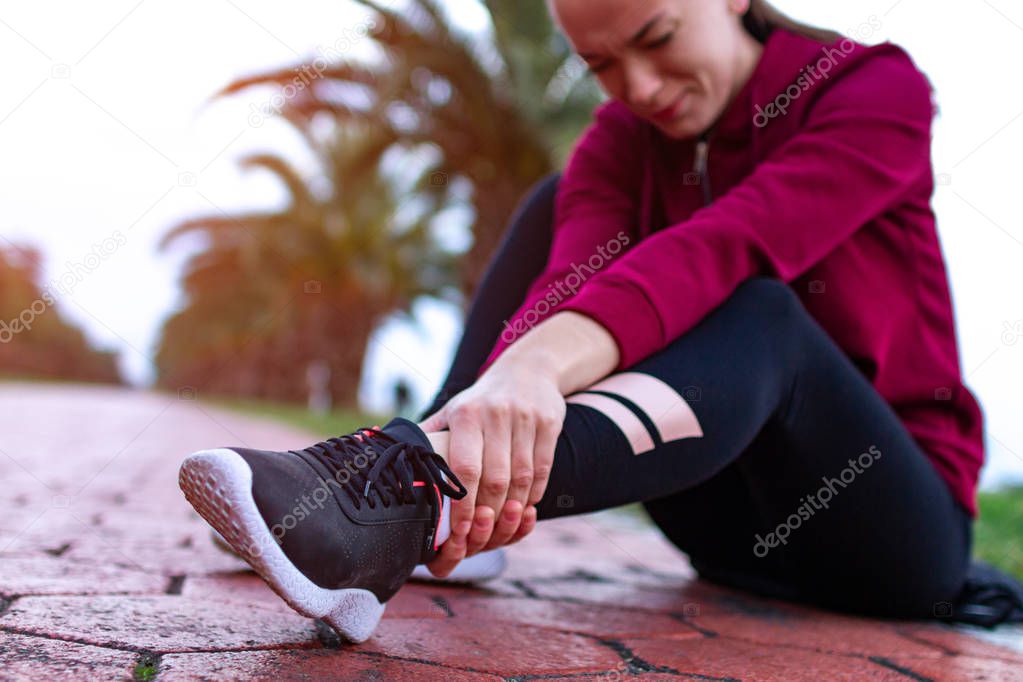 A young, fitness girl in sneakers and sportswear was injured while jogging and sports training. Leg injury and muscle strain, and ankle sprain accident during sports exercise. 