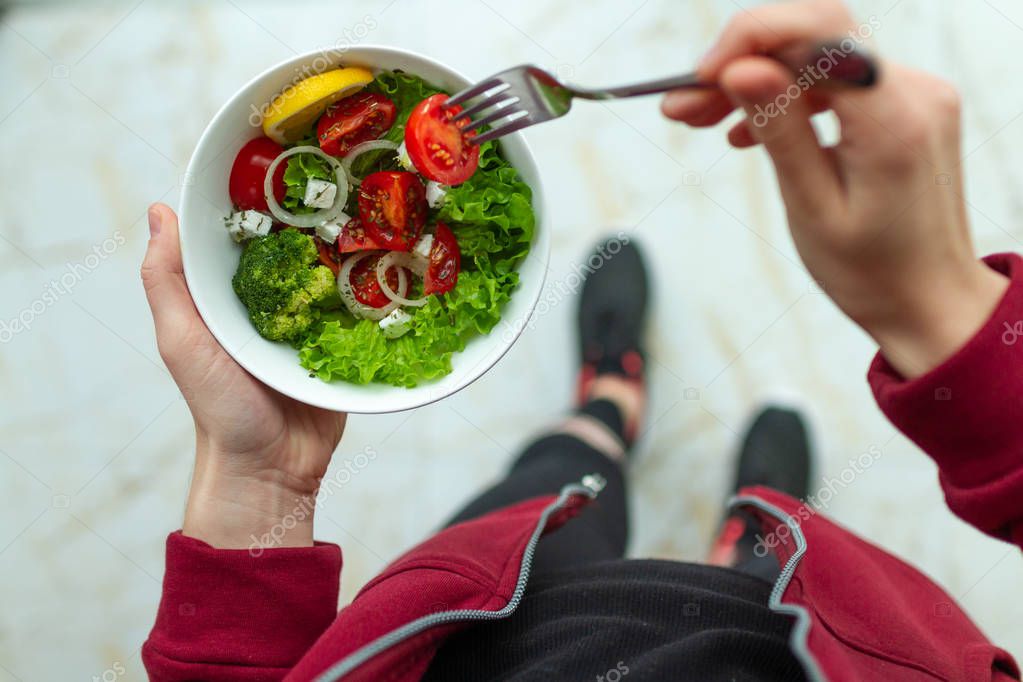 Young fitness woman in sneakers is eating a healthy salad after a workout. Fitness and healthy lifestyle concept. Top view 