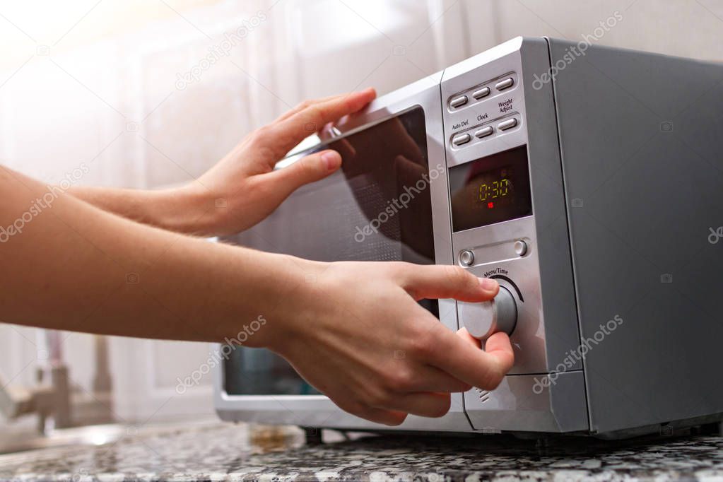 Woman's hand closing the door of the microwave oven and sets the time for heating food