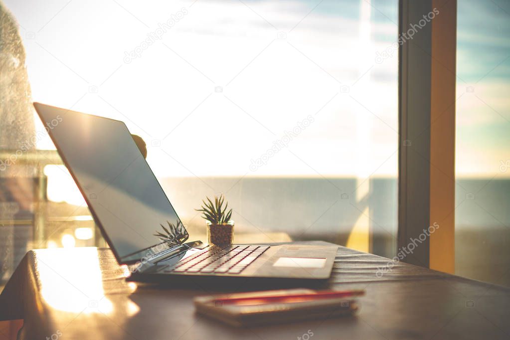 Cozy workplace in home office with laptop on table against the windows at sunset for online business, working, study. Remote work