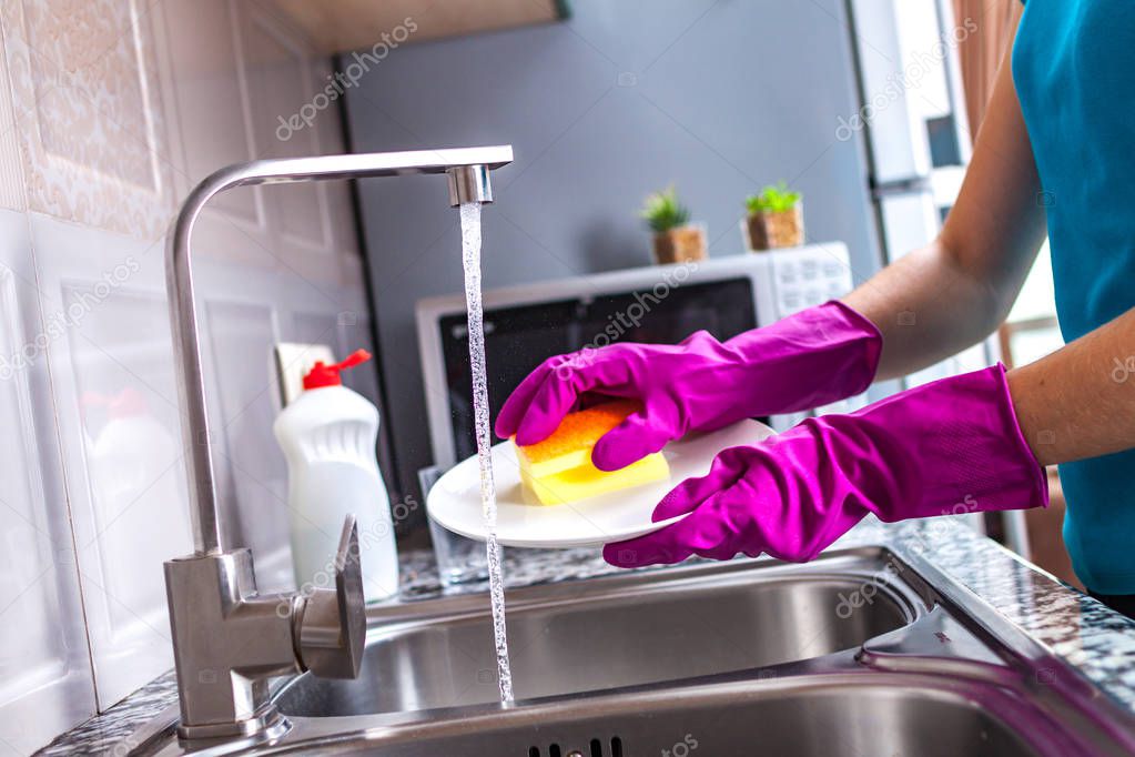 Housewife in rubber colored gloves washing dishes with a yellow sponge in the kitchen at home. 