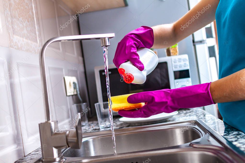 Housewife in rubber colored gloves washing dishes with a yellow sponge in the kitchen at home. 