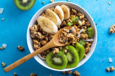 Kahvaltılık kuru. Dilim taze muz ve kivi mavi bir arka plan üzerinde ile müsli kase gevrek tatlım. Sağlıklı, fitness ve fiber yiyecek. Üstten Görünüm. Kahvaltı saati 