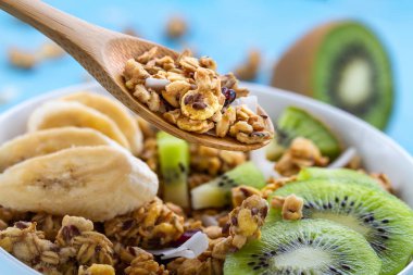 Kahvaltılık kuru. Dilim taze muz ve kivi mavi bir arka plan üzerinde beyaz bir kase müsli gevrek tatlım. Sağlıklı ve lif yiyecek. Kahvaltı saati 