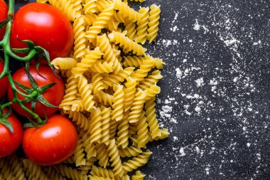 Siyah bir arka planda pişmiş düdük ve taze domates. İtalyan yemeği. Makarna pişirmek için malzemeler. Boşluk Kopyala. Üst görünüm