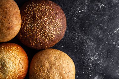 Siyah bir arka planda sarı ve kahverengi susam çörekler. Üst görünüm. Un ve unlu mamuller. Taze ekmek. Boşluk Kopyala 