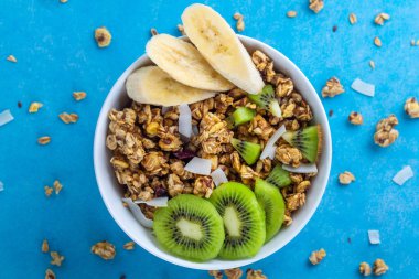 Kahvaltılık kuru. Dilim taze muz ve kivi mavi bir arka plan üzerinde ile müsli kase gevrek tatlım. Sağlıklı, fitness ve fiber yiyecek. Üstten Görünüm. Kahvaltı saati 