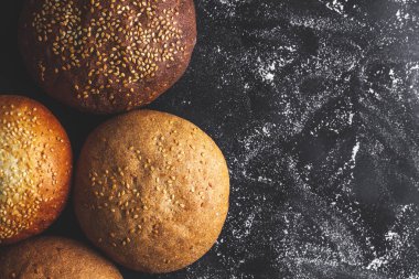 Siyah bir arka planda sarı ve kahverengi susam çörekler. Üst görünüm. Un ve unlu mamuller. Taze ekmek. Boşluk Kopyala 