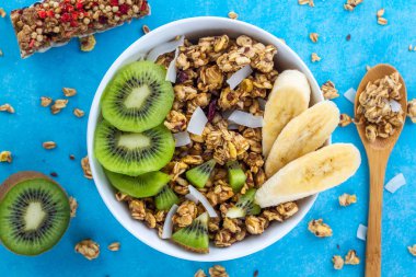 Kahvaltılık kuru. Dilim taze muz ve kivi mavi bir arka plan üzerinde ile müsli kase gevrek tatlım. Sağlıklı, fitness ve fiber yiyecek. Üstten Görünüm. Kahvaltı saati 
