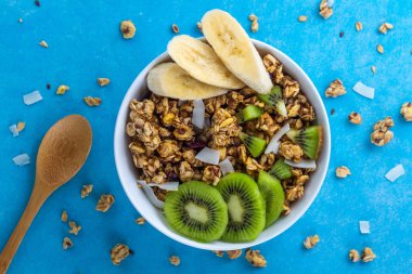 Kahvaltılık kuru. Dilim taze muz ve kivi mavi bir arka plan üzerinde ile müsli kase gevrek tatlım. Sağlıklı, fitness ve fiber yiyecek. Üstten Görünüm. Kahvaltı saati 