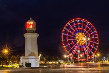 Akşamları yüksek, parlayan dönme dolabı ve deniz feneri. Batum, Gürcistan  