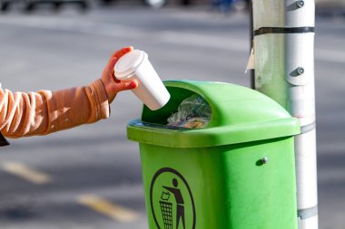 Kişi çöp kutusunda bir kağıt kahve bardağı dışarı atar. Şehirde sokakta çöp etmeyin