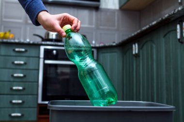 Mutfakta çöp kutusu içine boş plastik şişe atma bir kişinin yakın çekim. Plastik geri dönüşüm ve atık ayırma