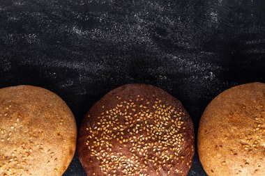 Siyah bir arka planda sarı ve kahverengi susam çörekler. Üst görünüm. Un ve unlu mamuller. Taze ekmek. Boşluk Kopyala 
