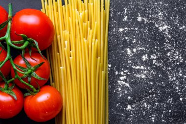 Pişmiş, Kurutulmuş spagetti ve siyah arka planda taze domates. İtalyan makarna pişirmek için malzemeler. Boşluk Kopyala. Üst görünüm 