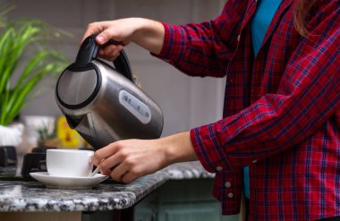 Bir insan bir elektrikli su ısıtıcısı kaynar sudan evde mutfak kullanarak çay yapıyor. Kahvaltı vakti