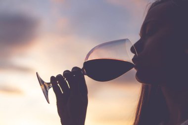 Rahatlatıcı, zevk ve akşam günbatımında bir kadeh şarap içmek genç bir kadın silüeti. 