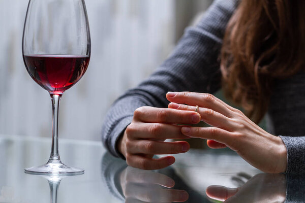 Divorced woman pulling wedding ring from finger and drinking a glass of a red wine because of adultery, betrayal and a failed marriage. Divorce concept. Relationship and love end. Life problems 