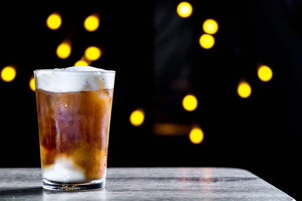 コーヒーの泡とライトの背景に氷で冷たいカクテル グラス — ストック写真