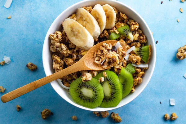 Dry breakfast cereals. Crunchy honey muesli bowl with slices of fresh banana and kiwi on a blue background. Healthy, fitness and fiber food. Top view