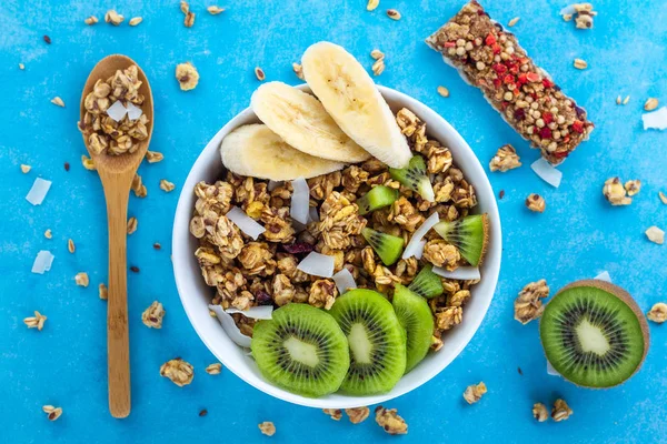 Dry breakfast cereals. Crunchy honey muesli bowl with slices of fresh banana and kiwi on a blue background. Healthy, fitness and fiber food. Top view. Breakfast time
