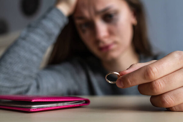 Разведенная женщина держит обручальное кольцо в руках и плачет, потому что
