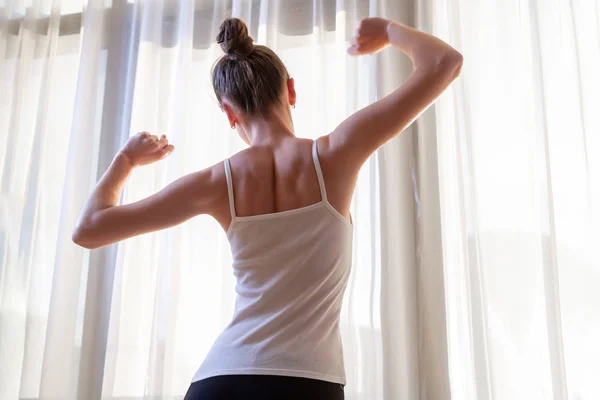 Young woman stretching near a window in apartment after wake up early in the morning. Start and the beginning a new day