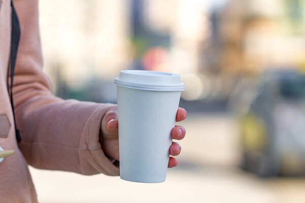 Young woman in casual clothes holding paper coffee cup and enjoying the walk in the city in the morning on a sunny day. Coffee away and to go 