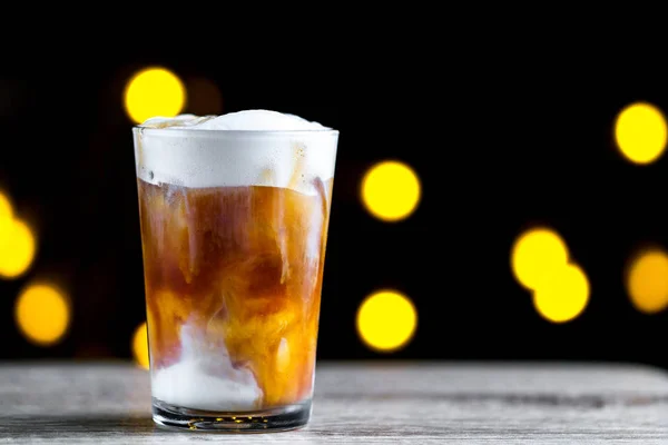 コーヒーの泡とライトの背景に氷で冷たいカクテル グラス — ストック写真