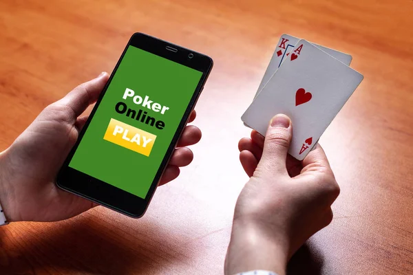 Close up of poker player with playing cards and smartphone in hands at the table. Online poker and gambling. Mobile poker app