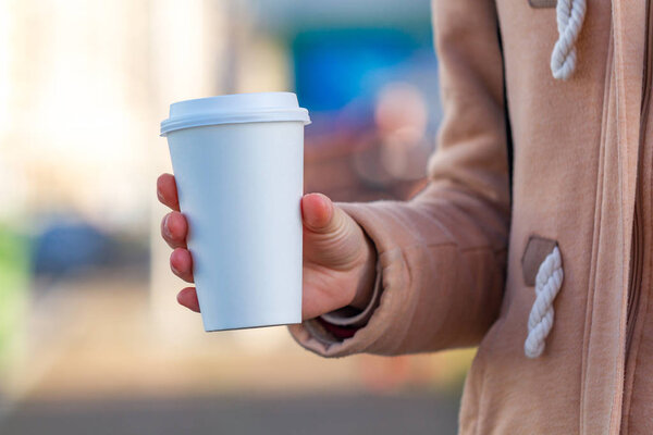 Young woman in casual clothes holding paper coffee cup and enjoying the walk in the city in the morning on a sunny day. Coffee away and to go 