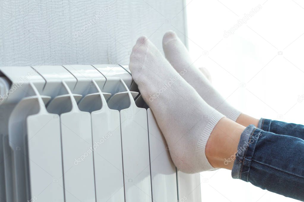 Young woman warming her legs on the battery at home 