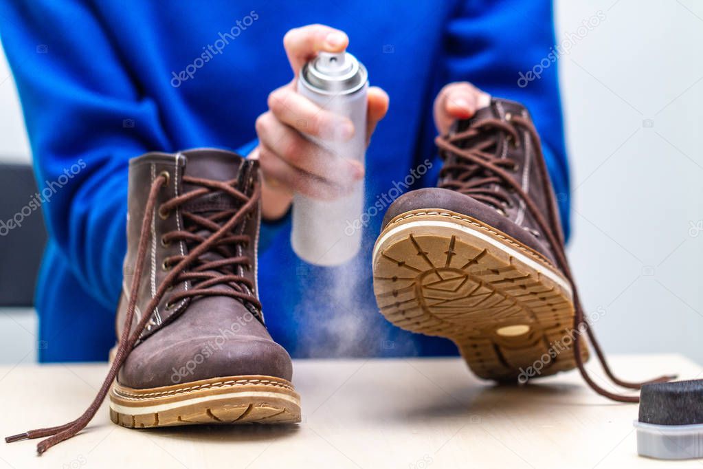 A person is cleaning and spraying agent on men's suede casual boots for protection from moisture and dirt. Shoe shine 