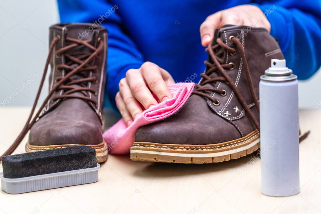 A person is cleaning men's suede casual boots with brush, rag and spray. Shoe shine. Footwear moisture and dirt protection