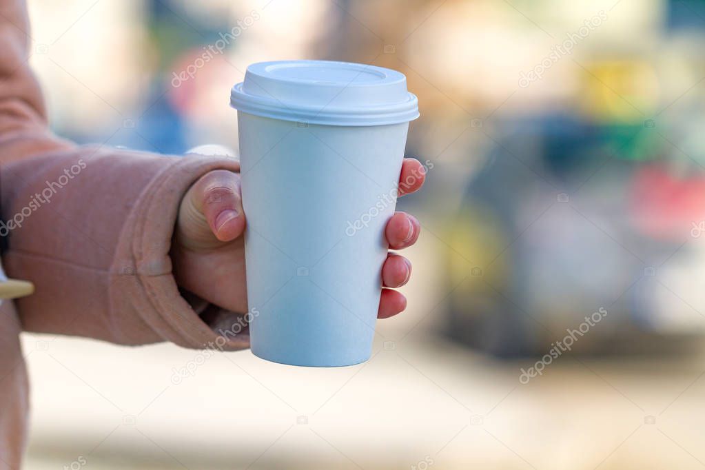Young woman in casual clothes holding paper coffee cup and enjoying the walk in the city in the morning on a sunny day. Coffee away and to go 