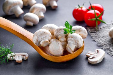 Beyaz mantarlar tahta kaşıkta maydanozlu, dereotlu, domatesli