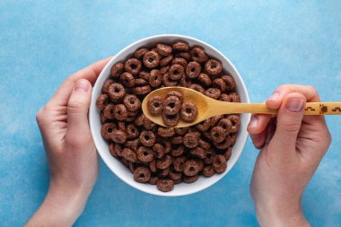 Çikolata, kahverengi, mavi arka plan üzerinde kuru kahvaltı için sırlı yüzük. Üst te. Tahıllar kaşık ve elinde kase