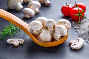 Beyaz mantarlar ahşap kaşıkta, dereotlu ve domatesli kirazlı, taze dilimlenmiş şampiyon ev yapımı yemekler yapıyor.