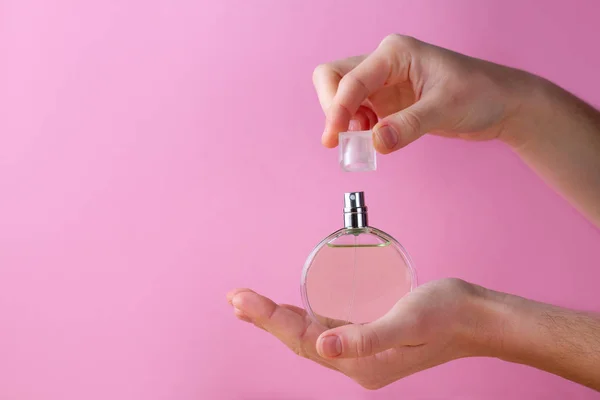 Botella de perfume de mujer en las manos sobre un fondo rosa . — Foto de Stock