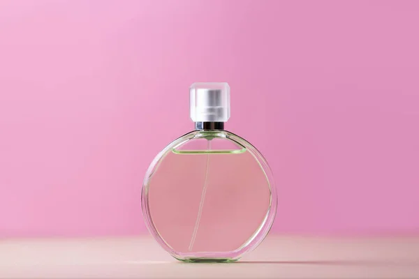 Glass bottle of perfume on pink background.