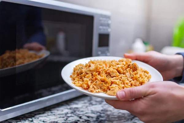 Bruke en mikrobølgeovn til å varme opp en tallerken med hjemmelaget pilaf til lunsj – stockfoto