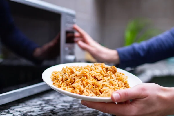 Bruke en mikrobølgeovn til å varme opp en tallerken med hjemmelaget pilaf til lunsj – stockfoto