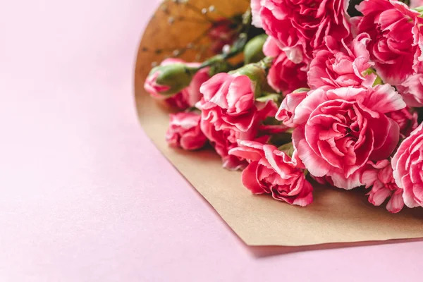 Ramo de flores frescas de clavel en papel artesanal sobre fondo rosa — Foto de Stock